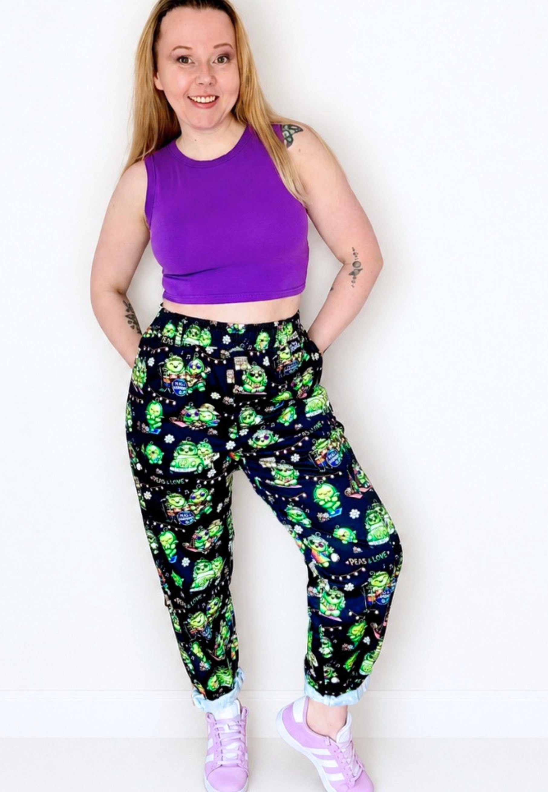 Woman wearing a purple top and black trousers which have a cute print of hippie peas at a peas festival. 