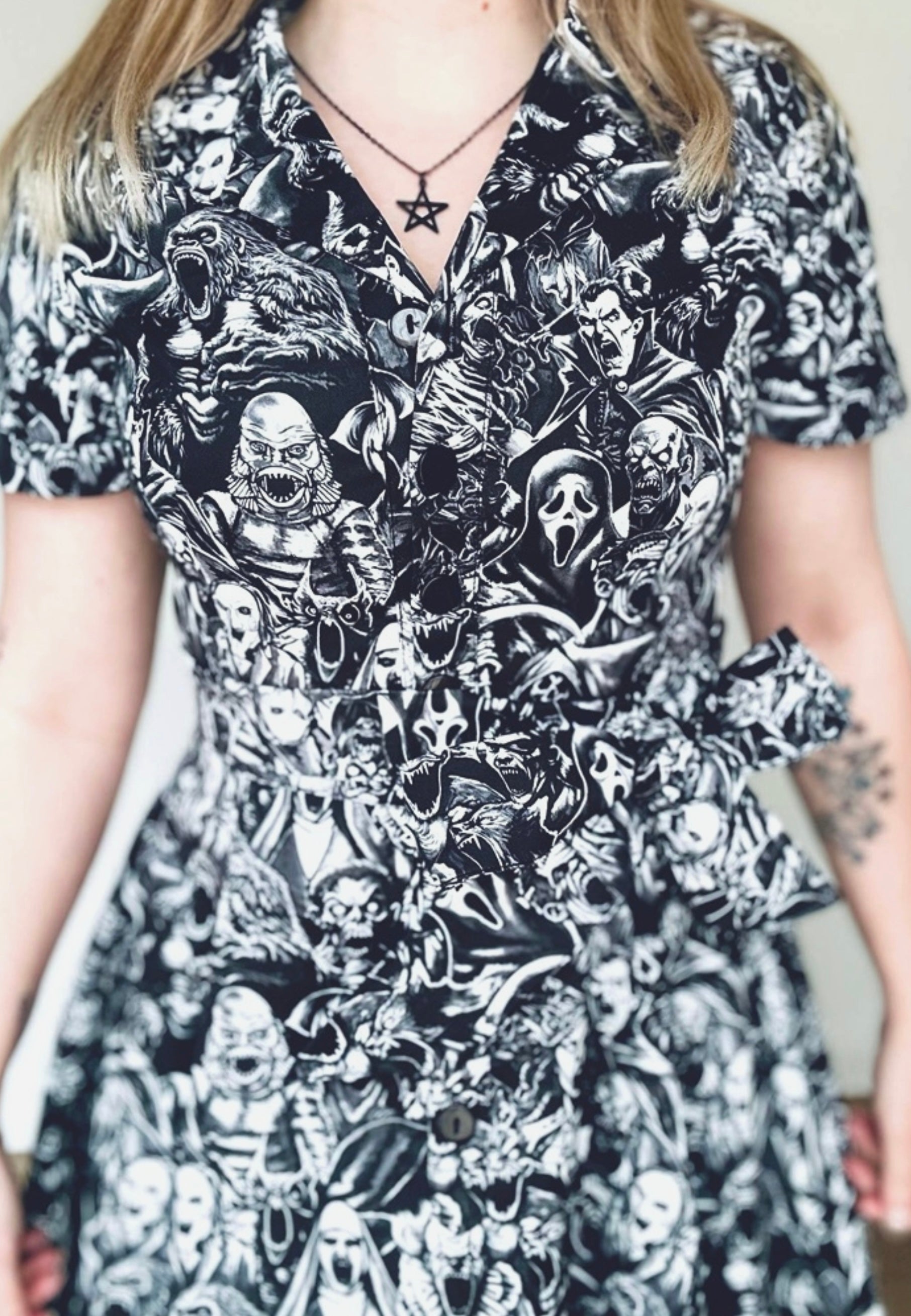 Woman wearing a retro style shirt dress with a gothic print in a grayscale of all the old school and modern monster, cryptoids and zombies all screaming. In the style of the old horror comics. Horror goth style dress.