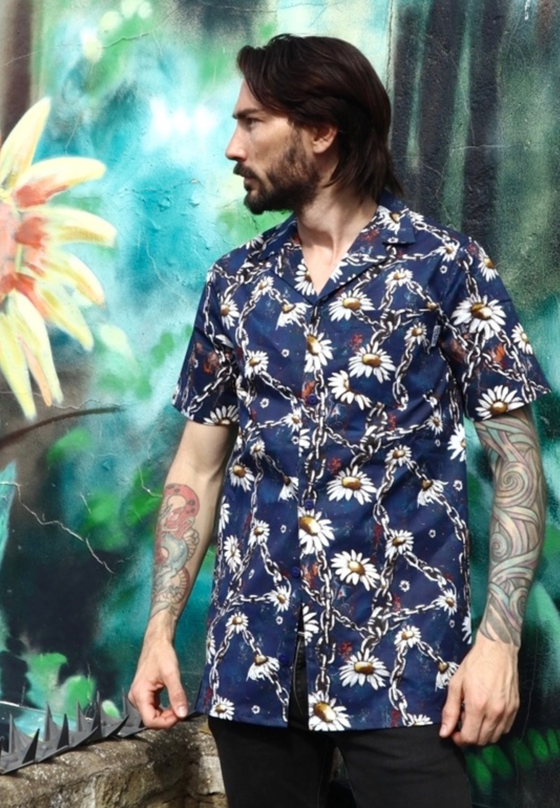 Man wearing a blue shirt with a daisy and urban grungey chains prong against a colorful mural background
