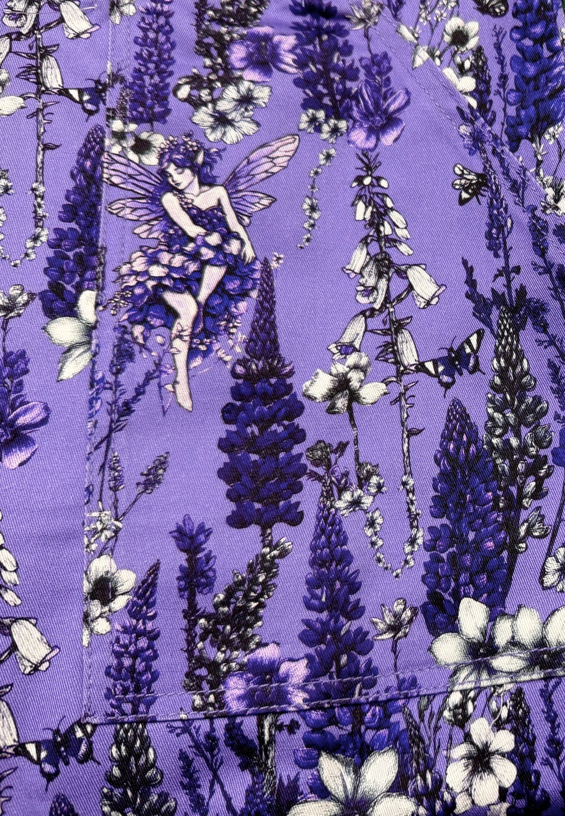 A close up of a purple fabric with a beautiful detailed print featuring wild flowers, fae and a butterfly. 
