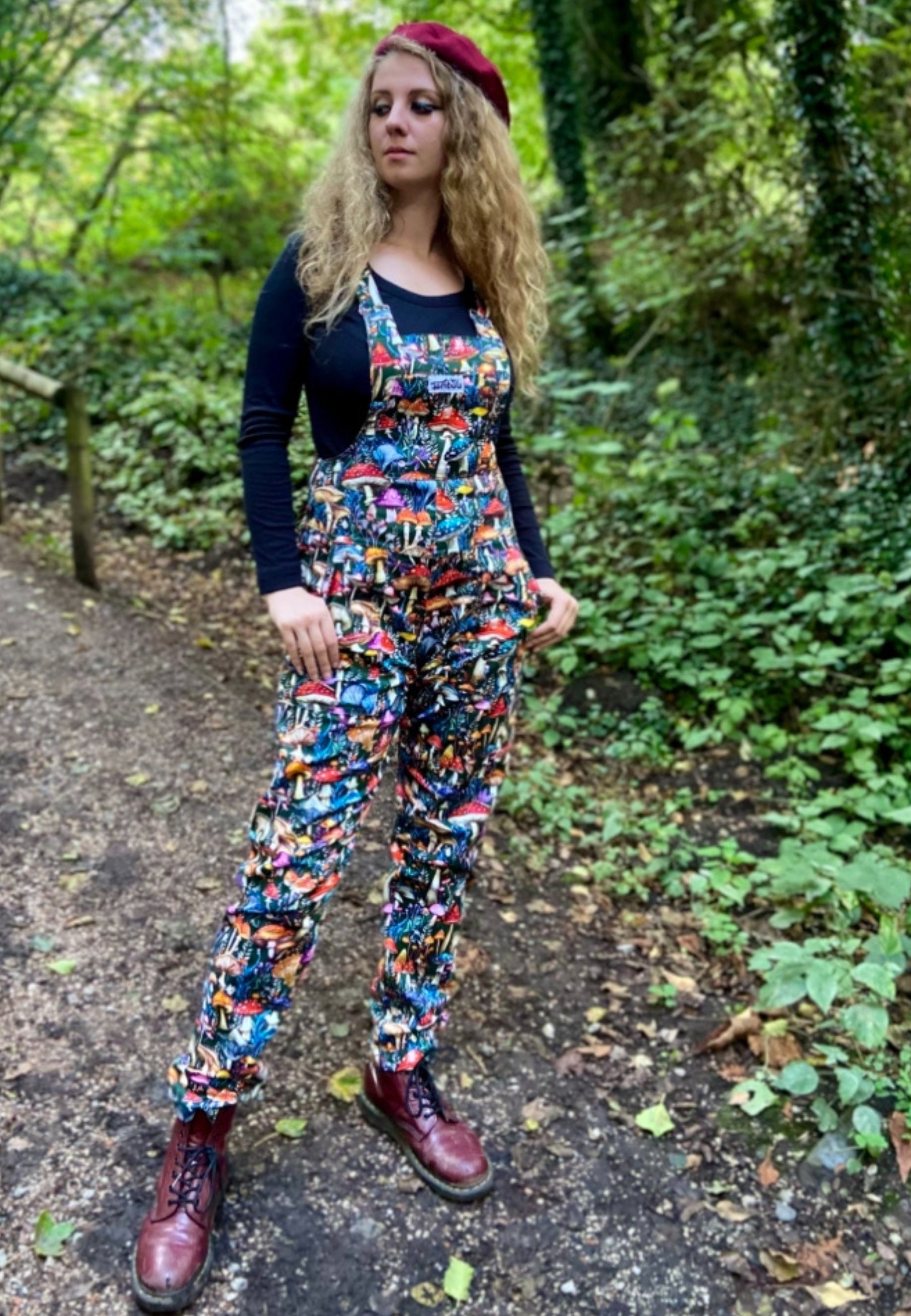 Woman wearing Jambats Wild Shrooms dungarees and a beret, standing on a forest path.