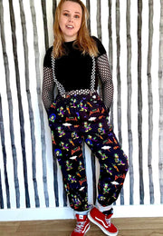 Woman wearing a black top and patterned trousers with a print of 80’s 90’s childhood character Court  Duckula against a striped wall.