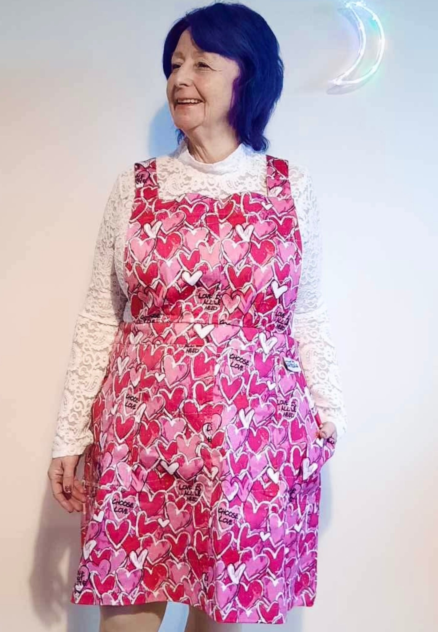 A woman wearing a pink pinafore dress with a pattern of scribbled hearts and love related graphics