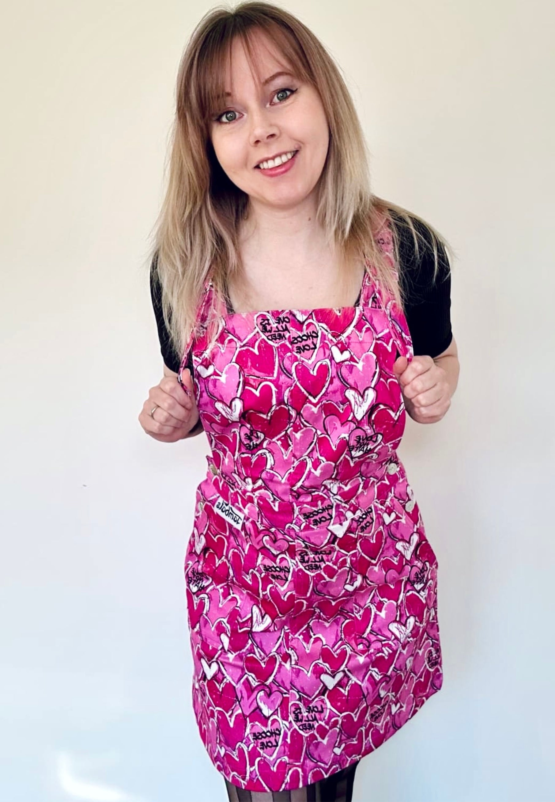 A woman wearing a pink pinafore dress with a pattern of scribbled hearts and love related graphics