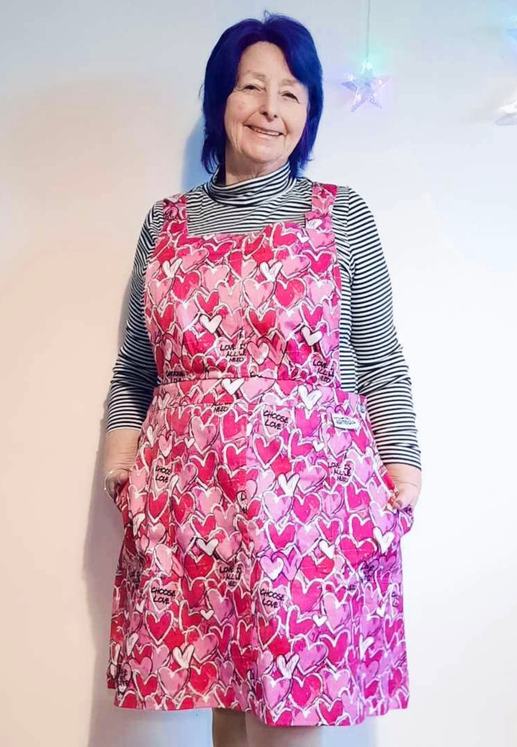 A woman wearing a pink pinafore dress with a pattern of scribbled hearts and love related graphics