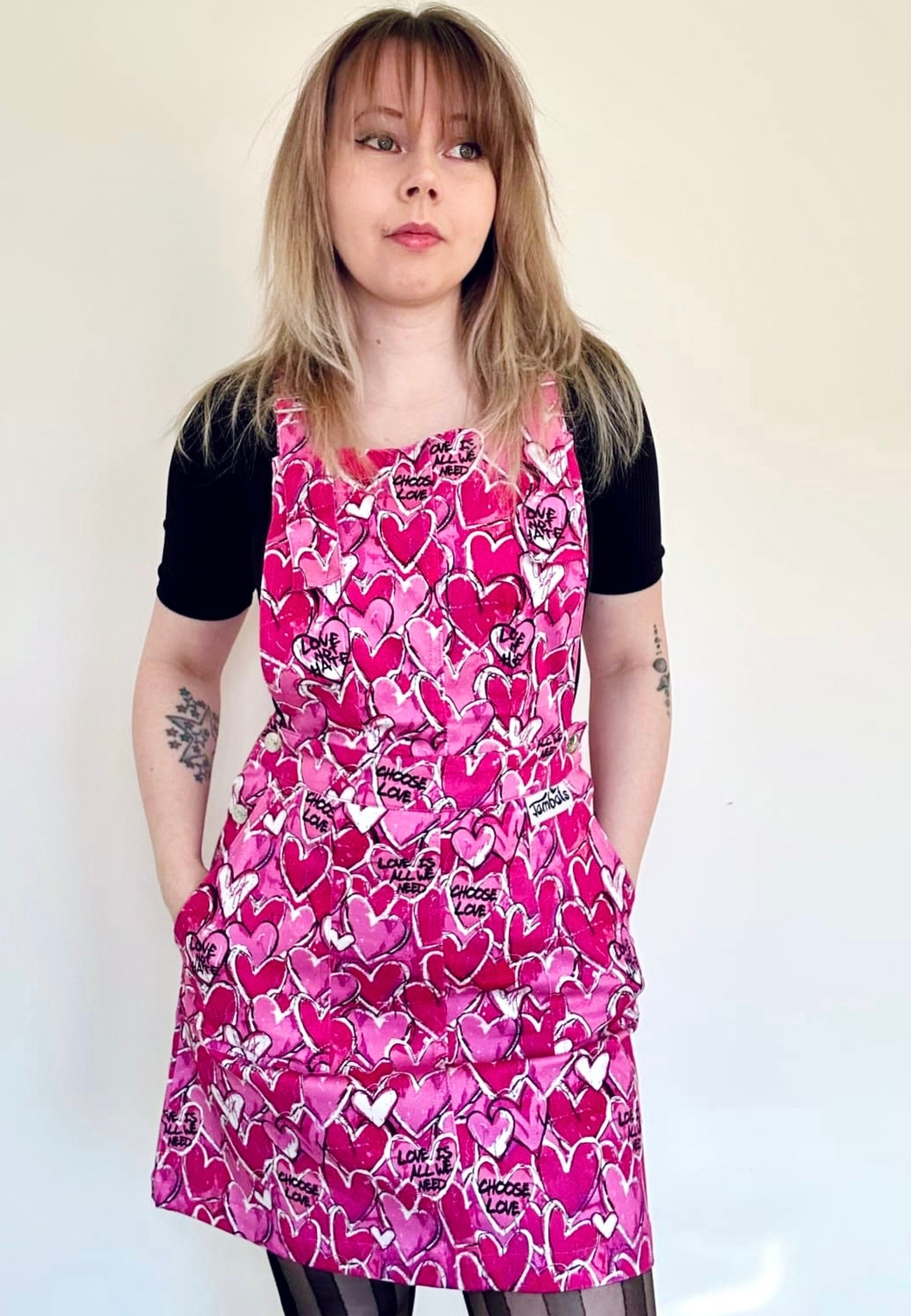 A woman wearing a pink pinafore dress with a pattern of scribbled hearts and love related graphics.