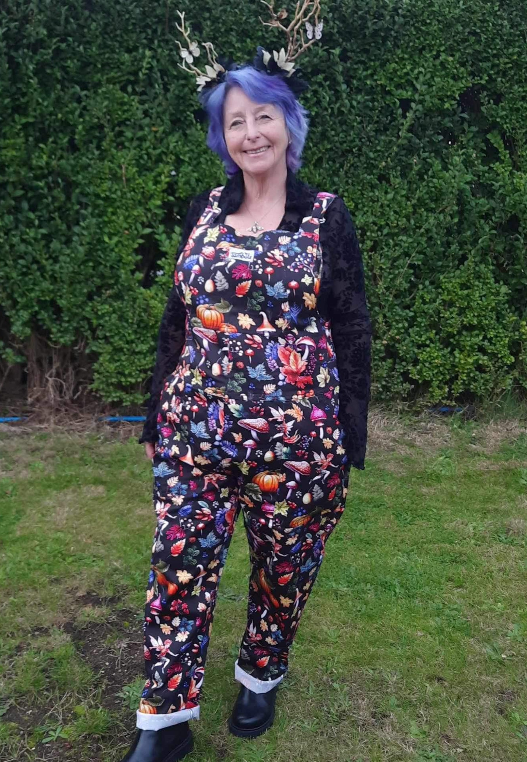 Woman wearing dungarees in a magical Autumnal Fae print. Beautiful whimsical Fae dungarees. 