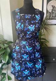 A pinafore dress featuring a moon and Luna moth pattern, predominantly dark colour background with vibrant blues and turquoise , displayed on a mannequin.