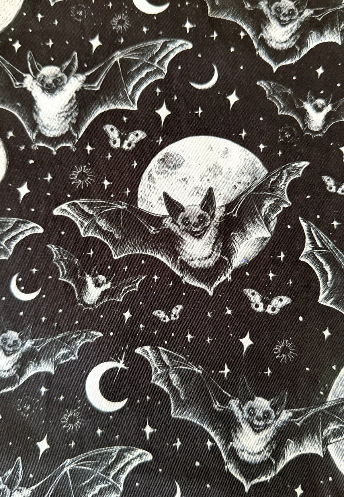 Black fabric with a repeating white and gray print of bats flying around a full moon and stars.
