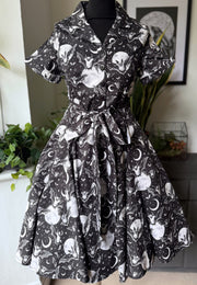 A short sleeve button front dress displayed on a mannequin indoors. The dress has a black base with a gothic print featuring bats, moons and stars.