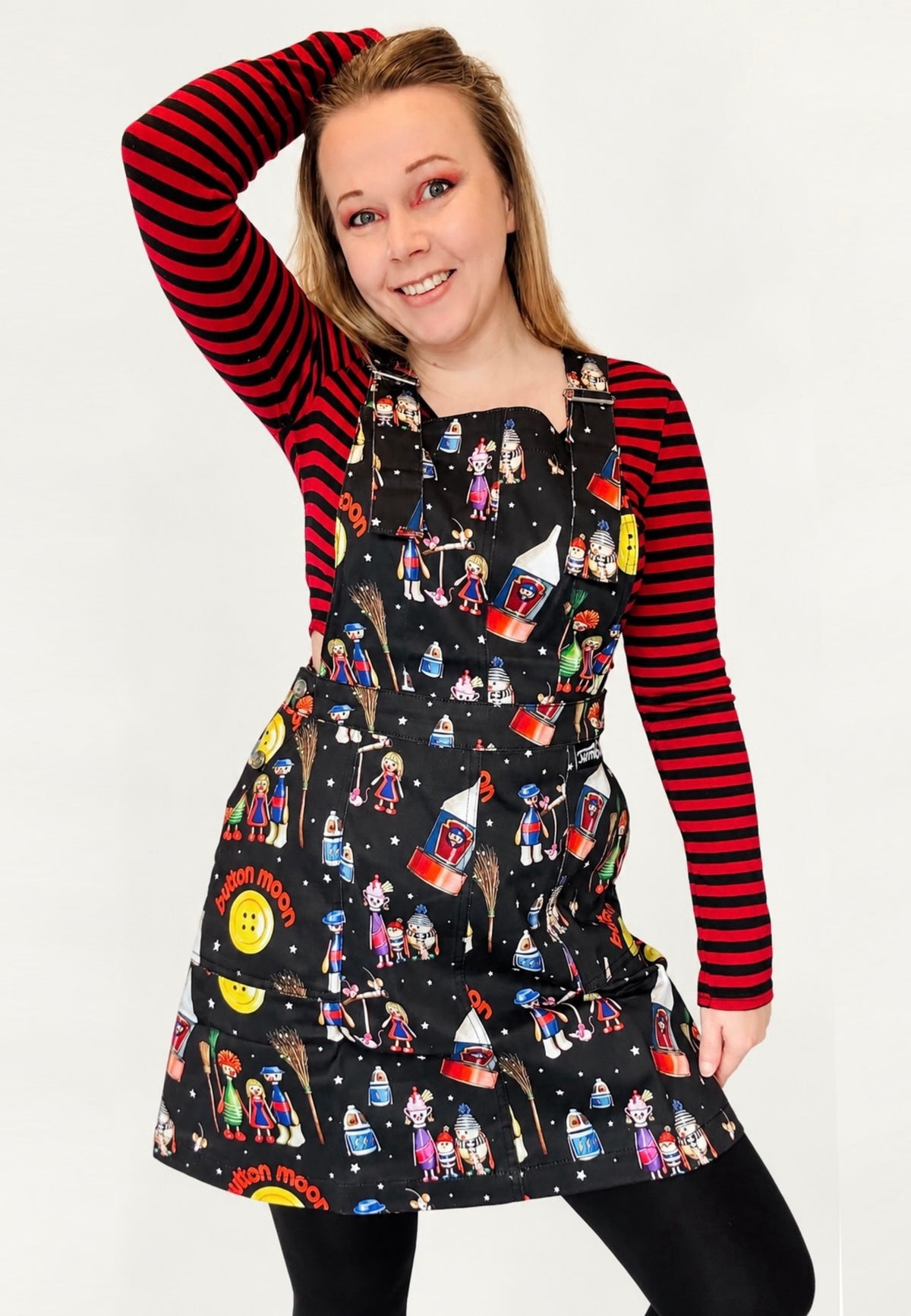 Woman wearing a retro nostalgic pinafore with a Button Moon print over a red and black on striped top on a white background 