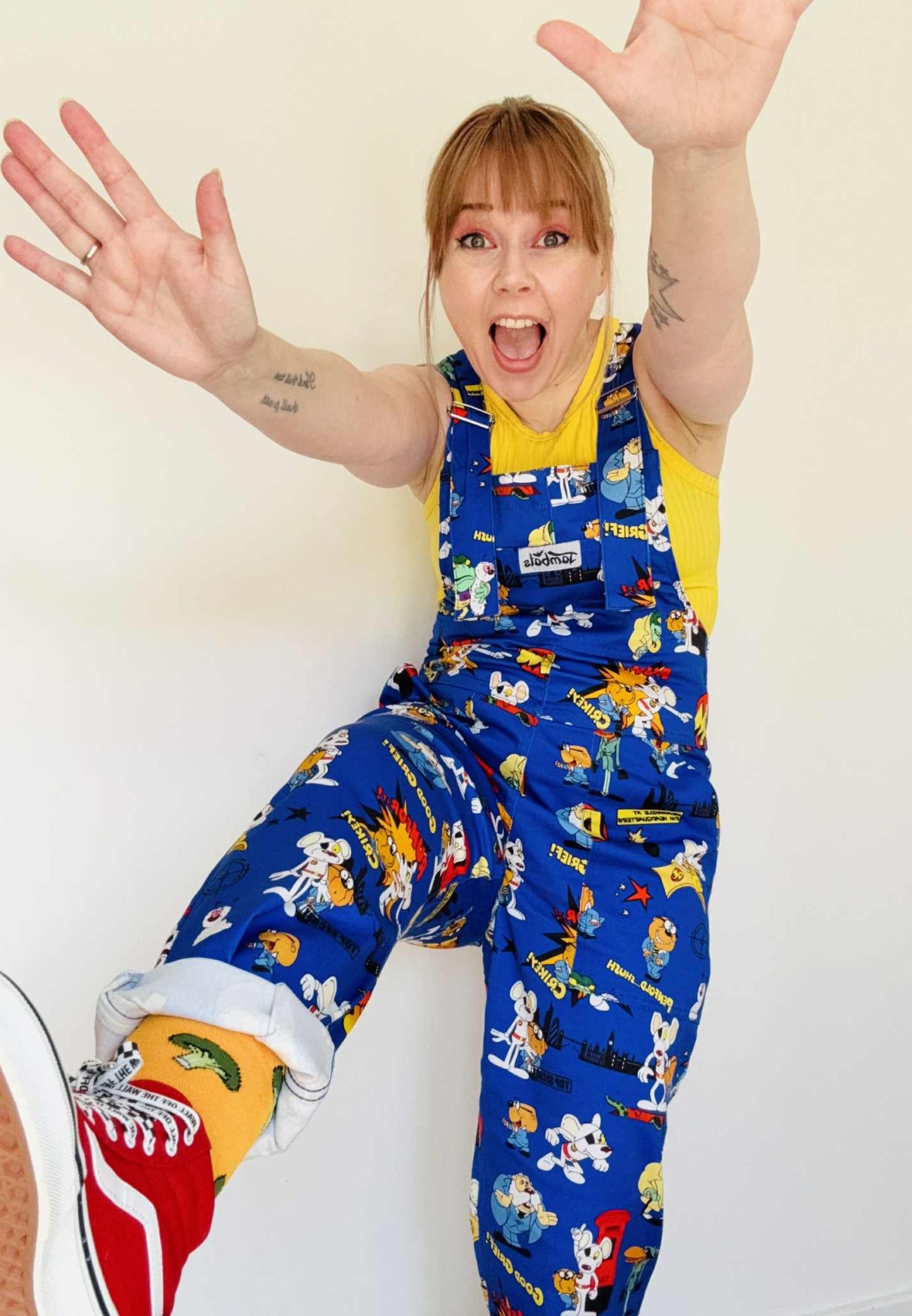 Woman wearing blue Danger Mouse dungarees with a yellow top underneath. Studio photo