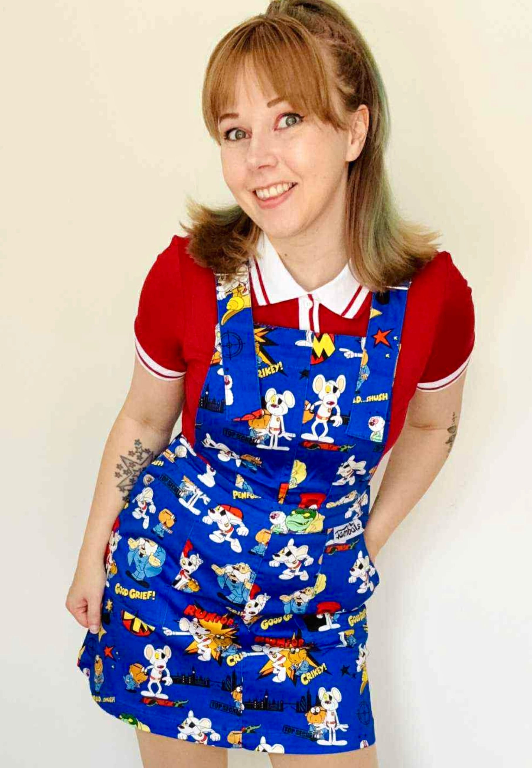 Woman wearing a blue Jambats pinafore dress with the retro 80s cartoon characters DangerMouse on the print. Officially licensed. DM.