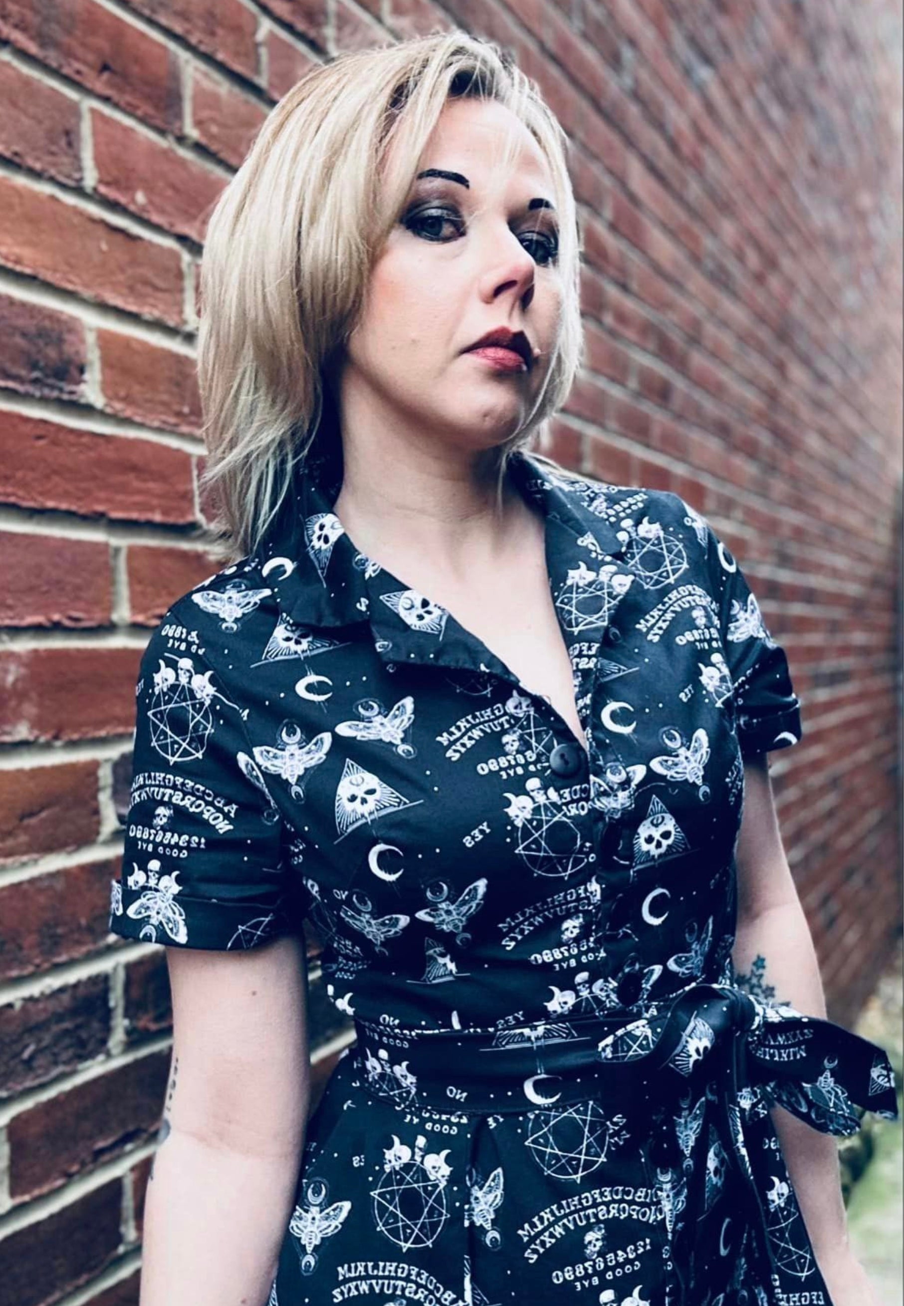 Close up image of woman wearing a black gothic Ouija print dress with a full skirt and button bodice.