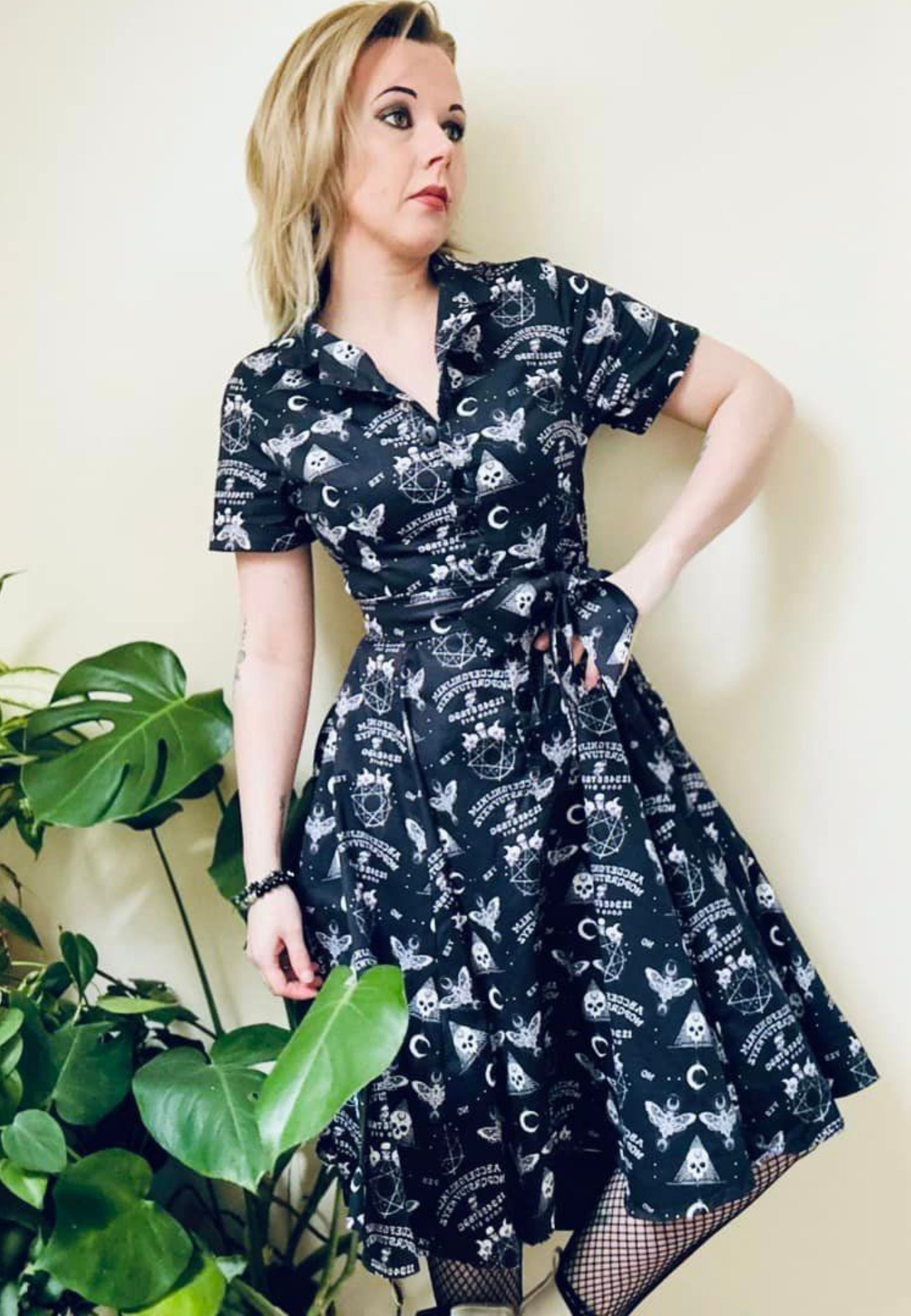 A woman wearing a black gothic Ouija print dress with a full skirt and button bodice.