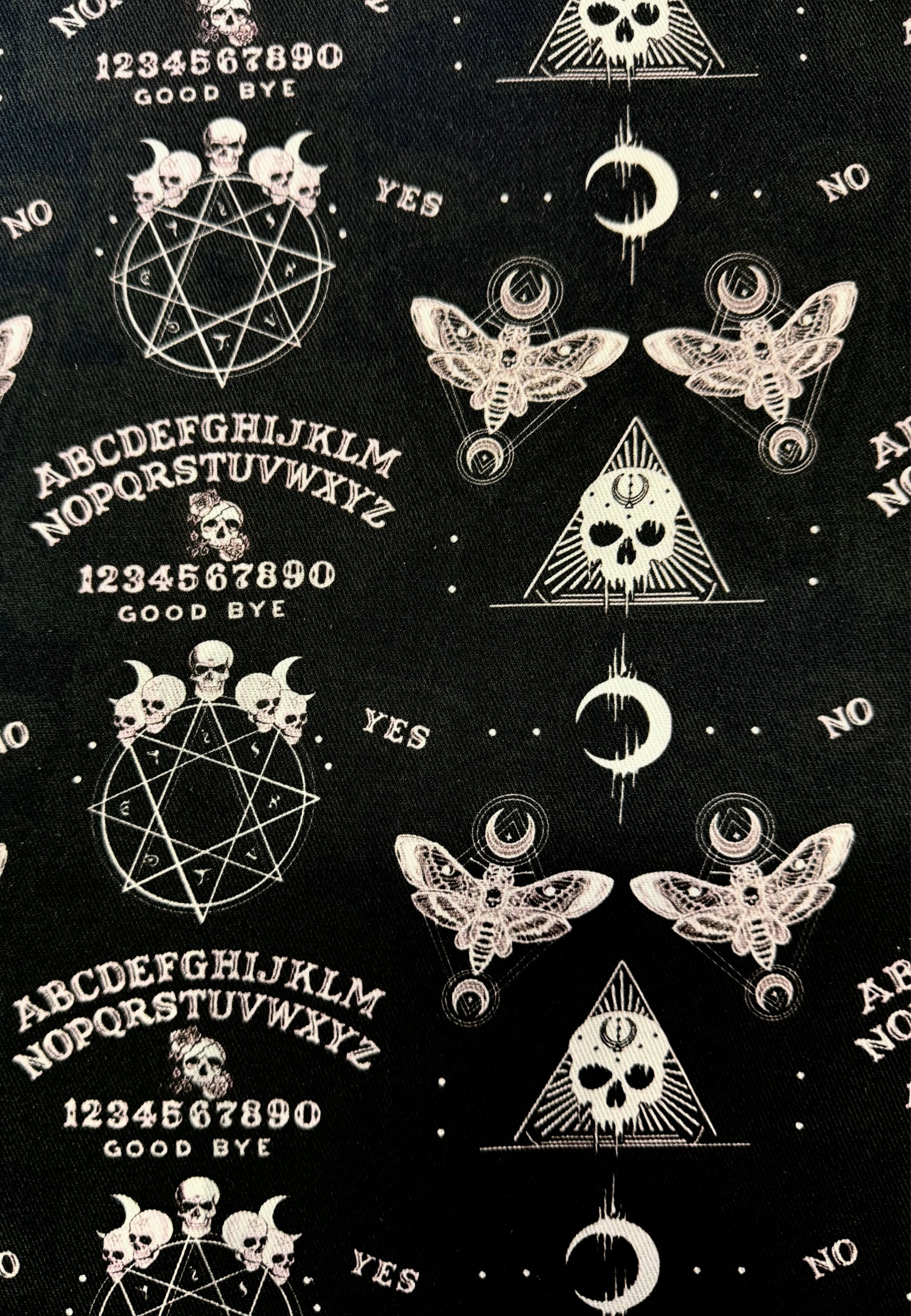 Close up of ouija print fabric. Black background with white ouija and gothic imagery and symbols