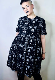 Woman wearing a black smock dress with gothic Ouija print pattern against a plain background. Studio photo 