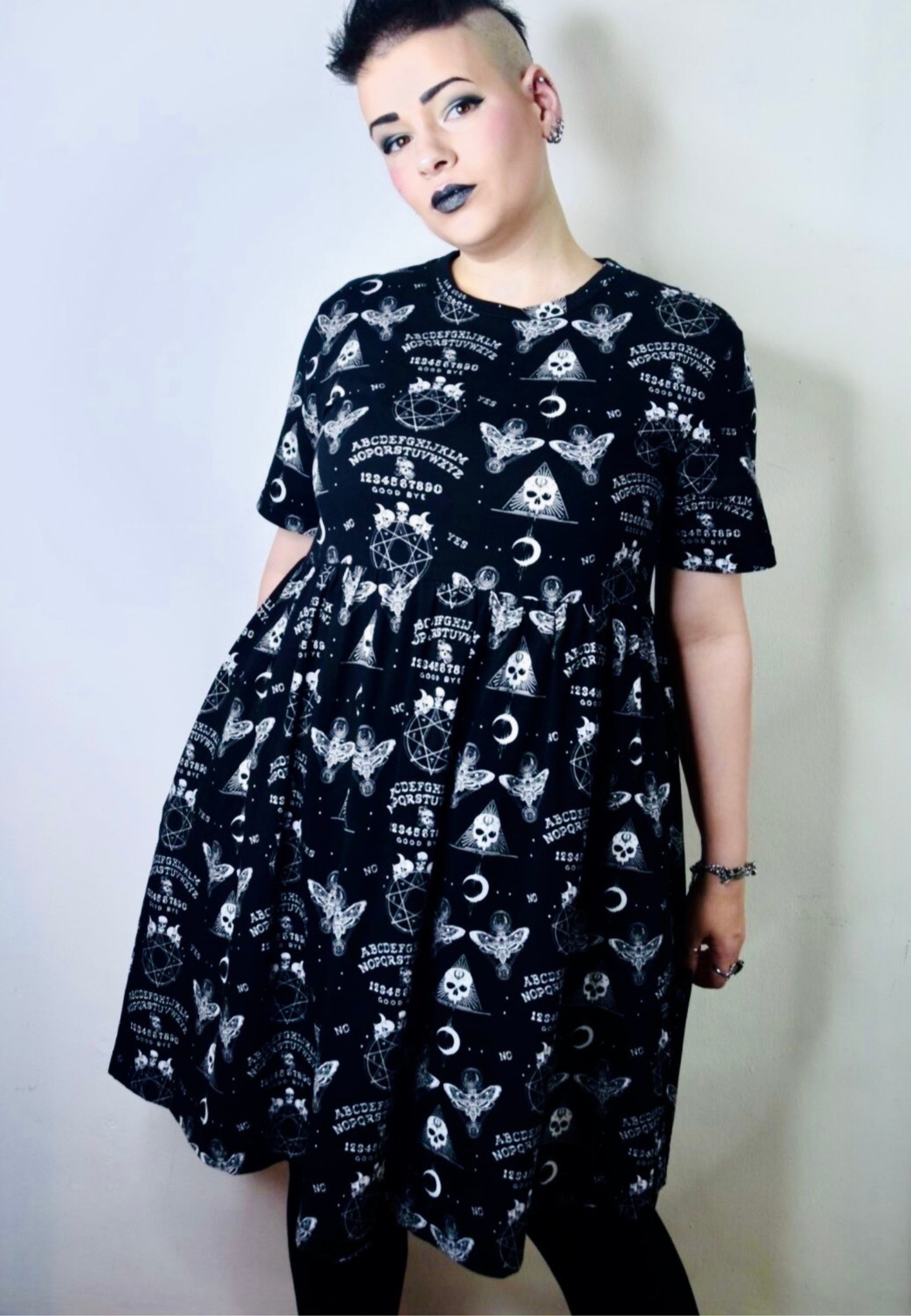 Woman wearing a black smock dress with gothic Ouija print pattern against a plain background. Studio photo 