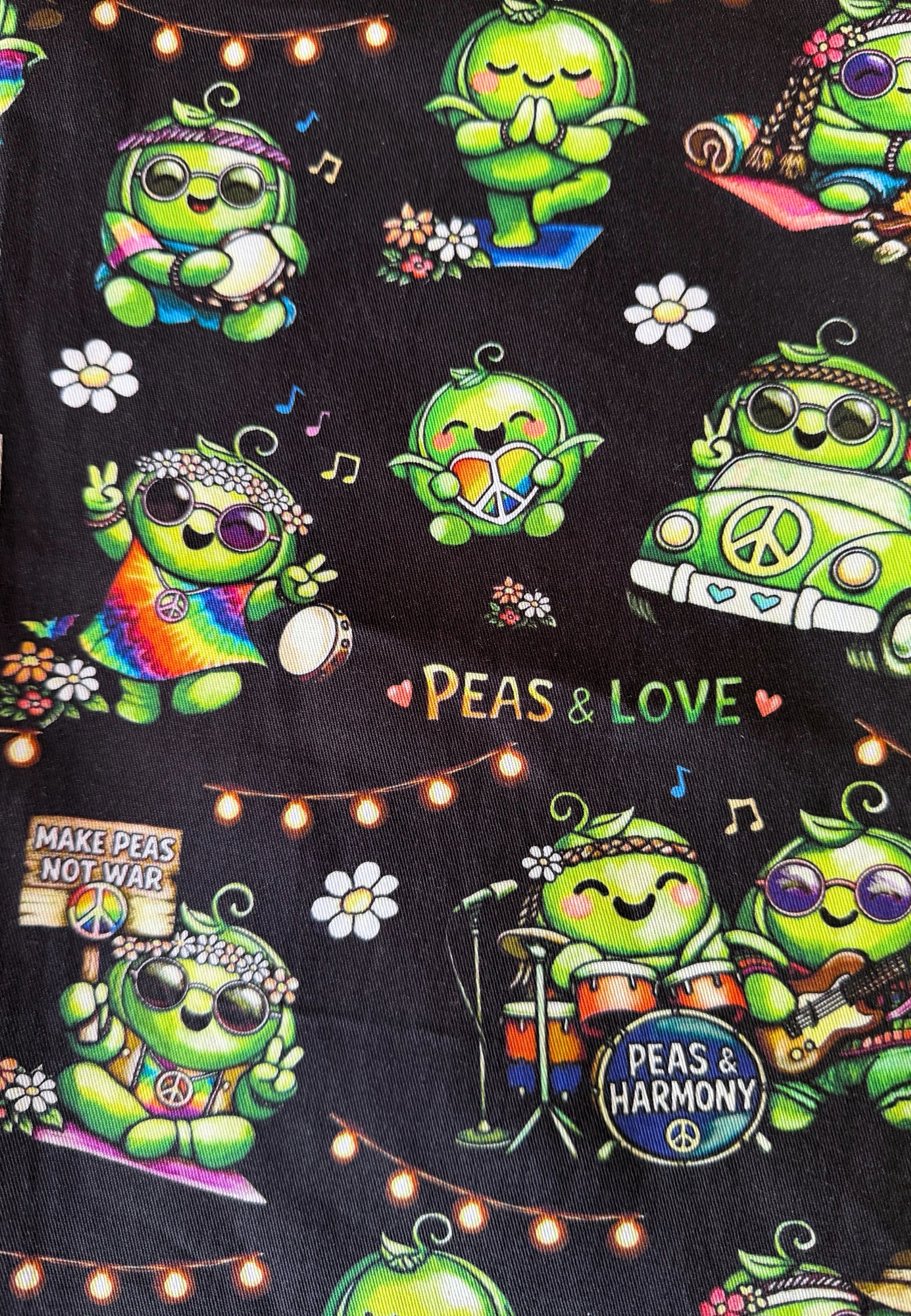 A close-up of a black fabric featuring a colorful retro pattern of green cartoon peas playing music, driving a white van, and surrounded by flowers, musical notes, and the text 'PEAS & LOVE'.