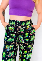 Person wearing a purple top and black trousers with green hippie peas at a Peas Festival print. 