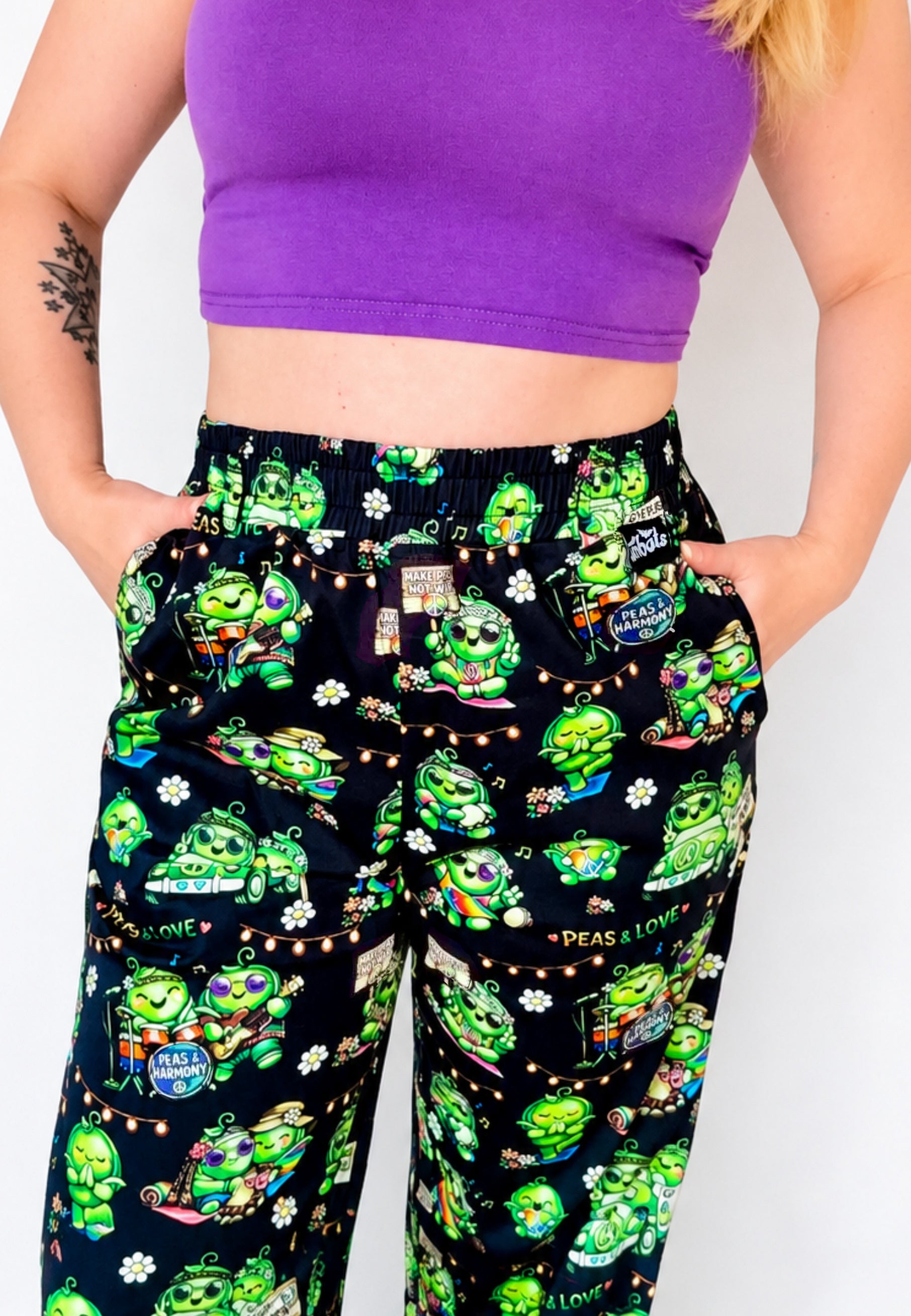 Person wearing a purple top and black trousers with green hippie peas at a Peas Festival print. 