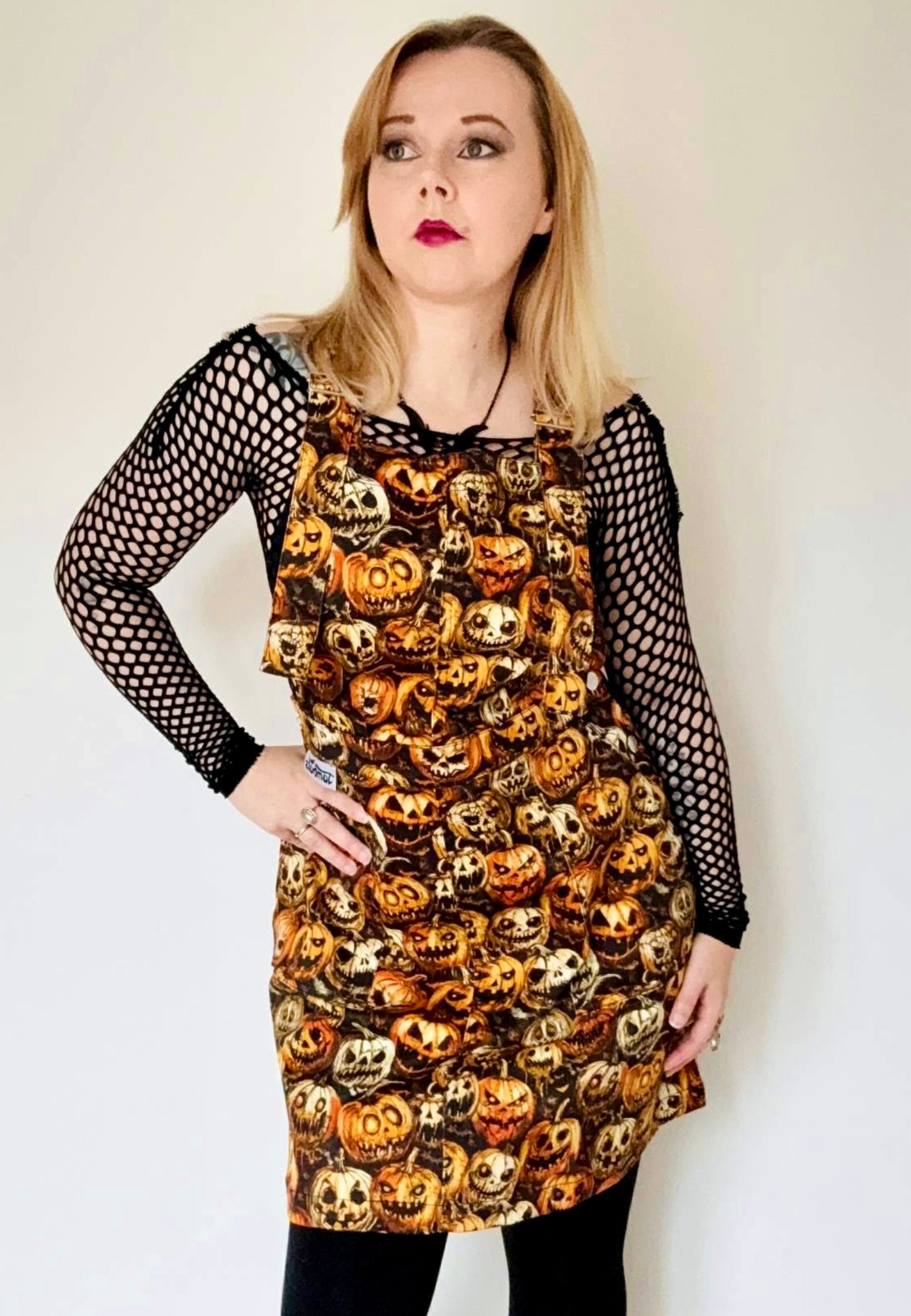 Woman wearing a spooky pinafore dress with creepy pumpkins print. Studio photo. 