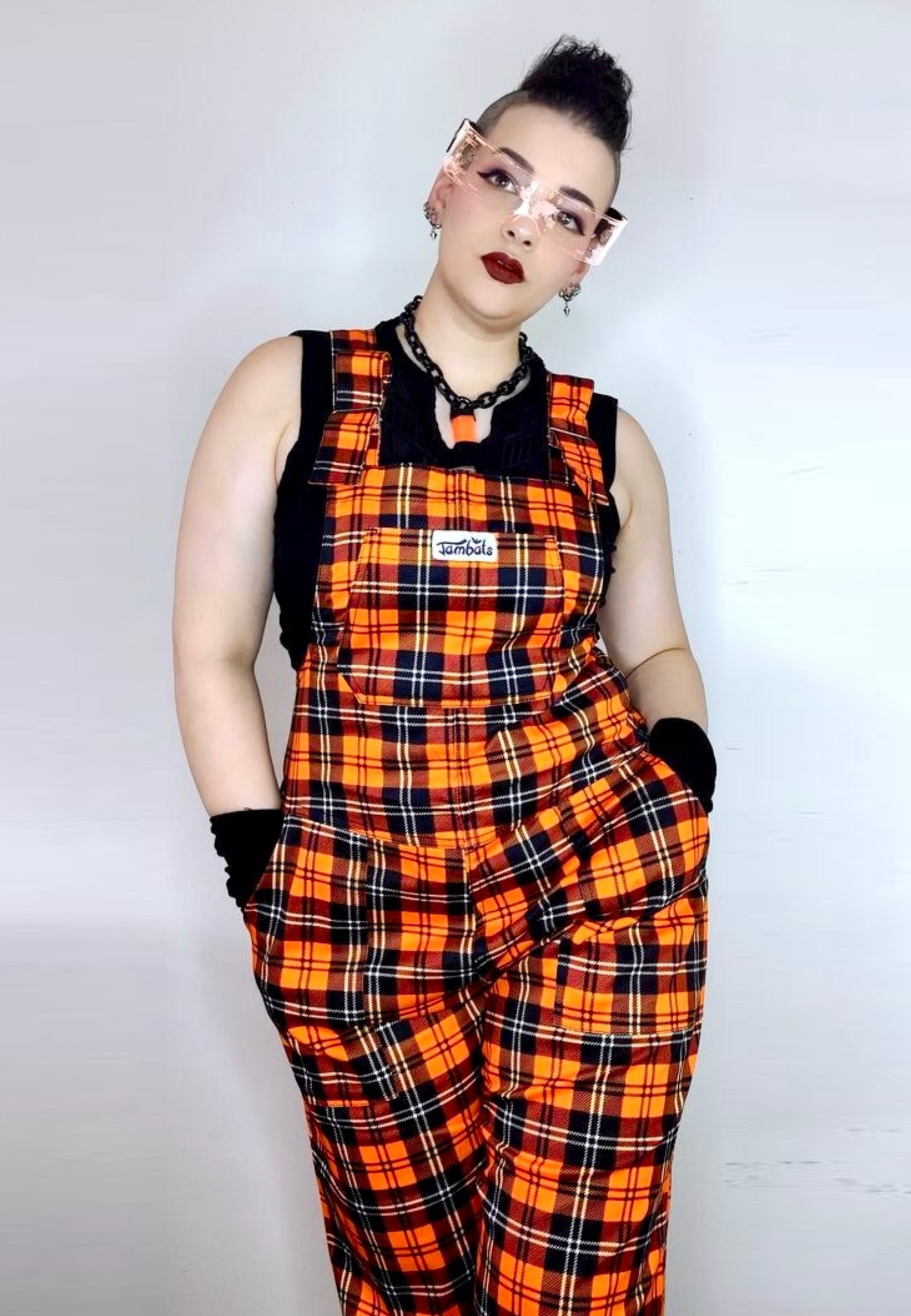 Woman wearing orange dungarees with a black sleeveless jacket on a white background. Punky alternative style