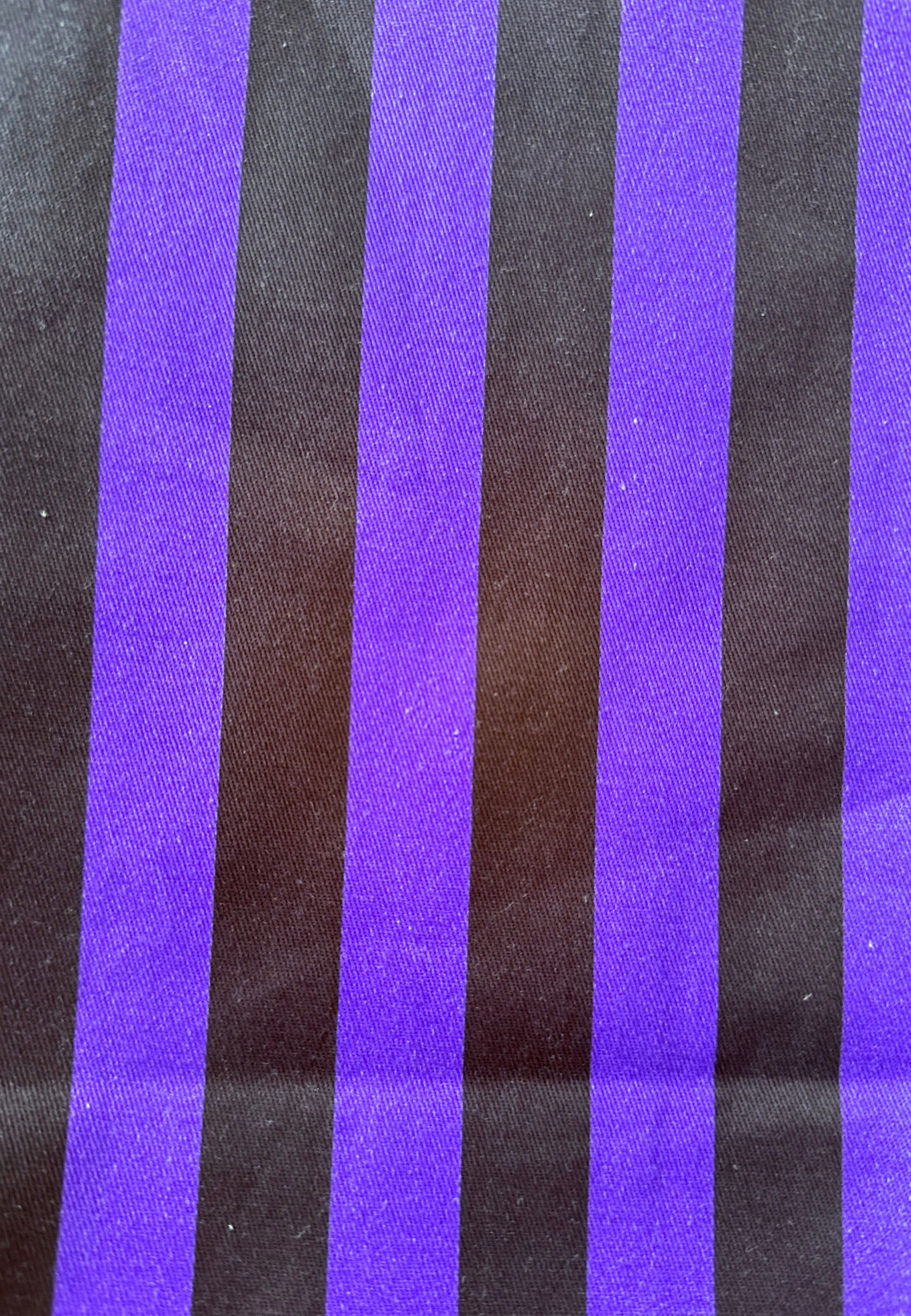 A close-up of a striped fabric or material with alternating wide purple and black vertical stripes.
