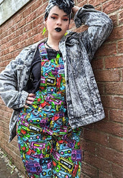 A woman wearing a colourful, vintage themed outfit with a pattern on dungarees of retro cassette tapes in a street art style. Styling is 80s pop culture style. 