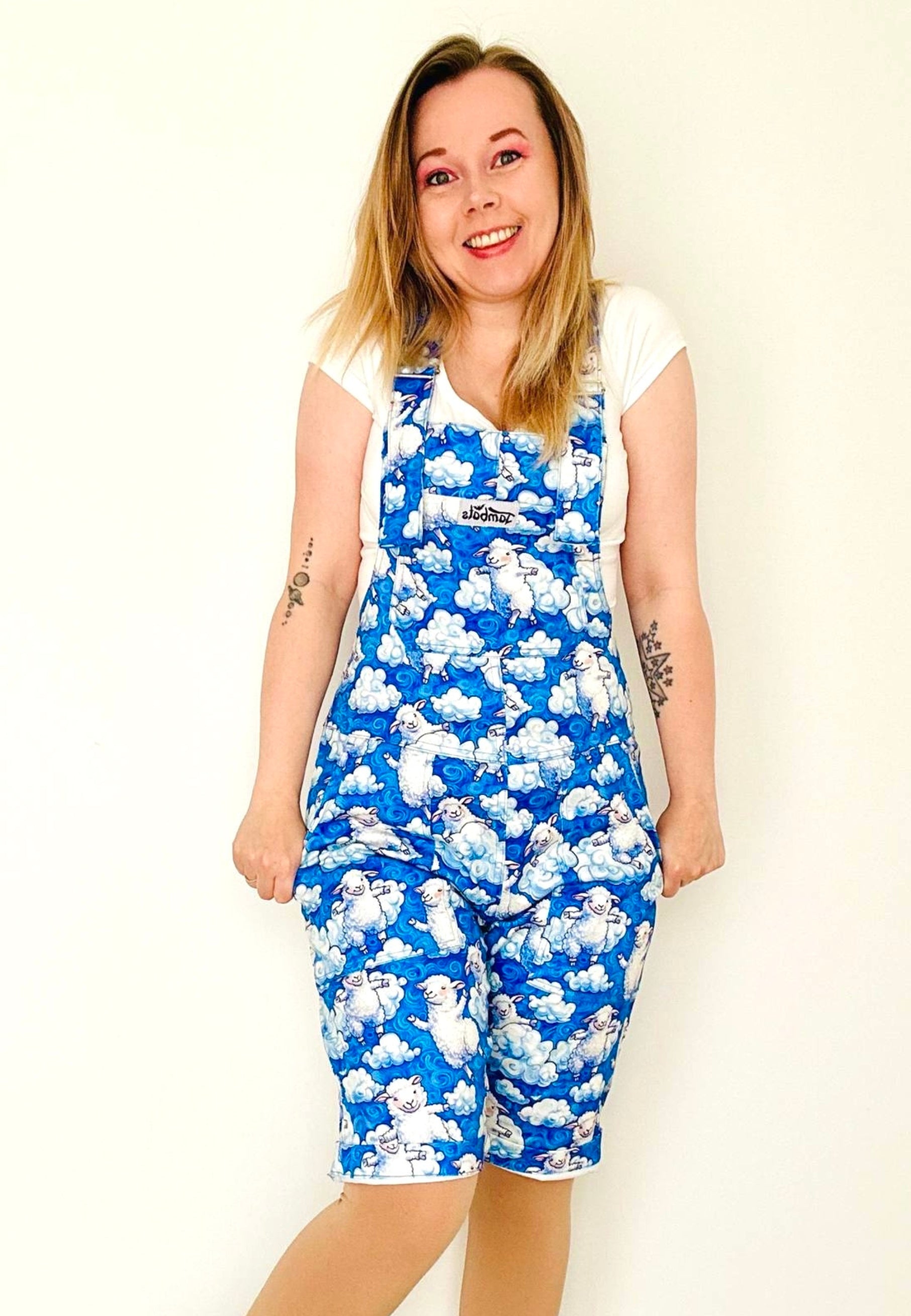 Model wearing a blue and white fluffy cloud and sheep dungarees. Studio photo on a plain background. Sheep cloud overall shorts. 