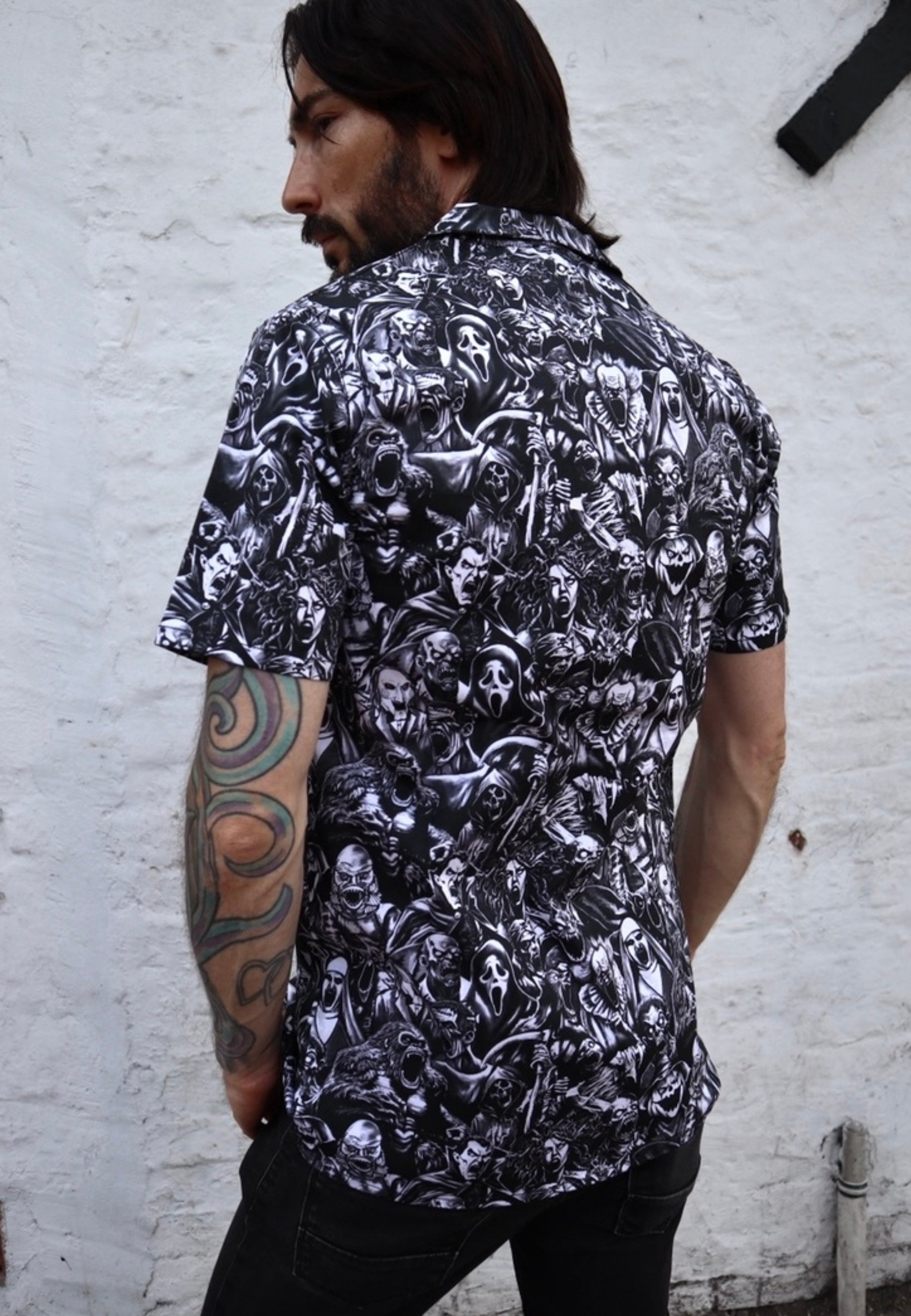 Back view of a man wearing a shirt with a gothic print in a grayscale of all the old school monster, cryptoids and zombies all screaming. In the style of the old horror comics. Horror goth style unisex shirt.