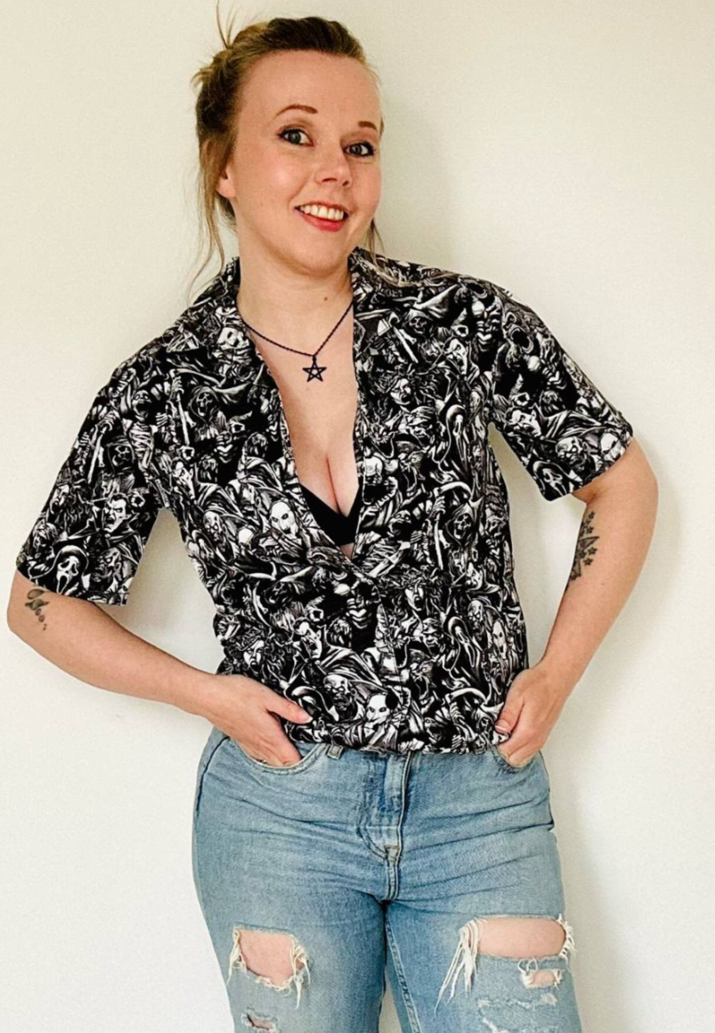 Woman wearing a shirt with a gothic print in a grayscale of all the old school monster, cryptoids and zombies all screaming. In the style of the old horror comics. Horror goth style unisex shirt. Woman also wearing ripped jeans with the shirt.