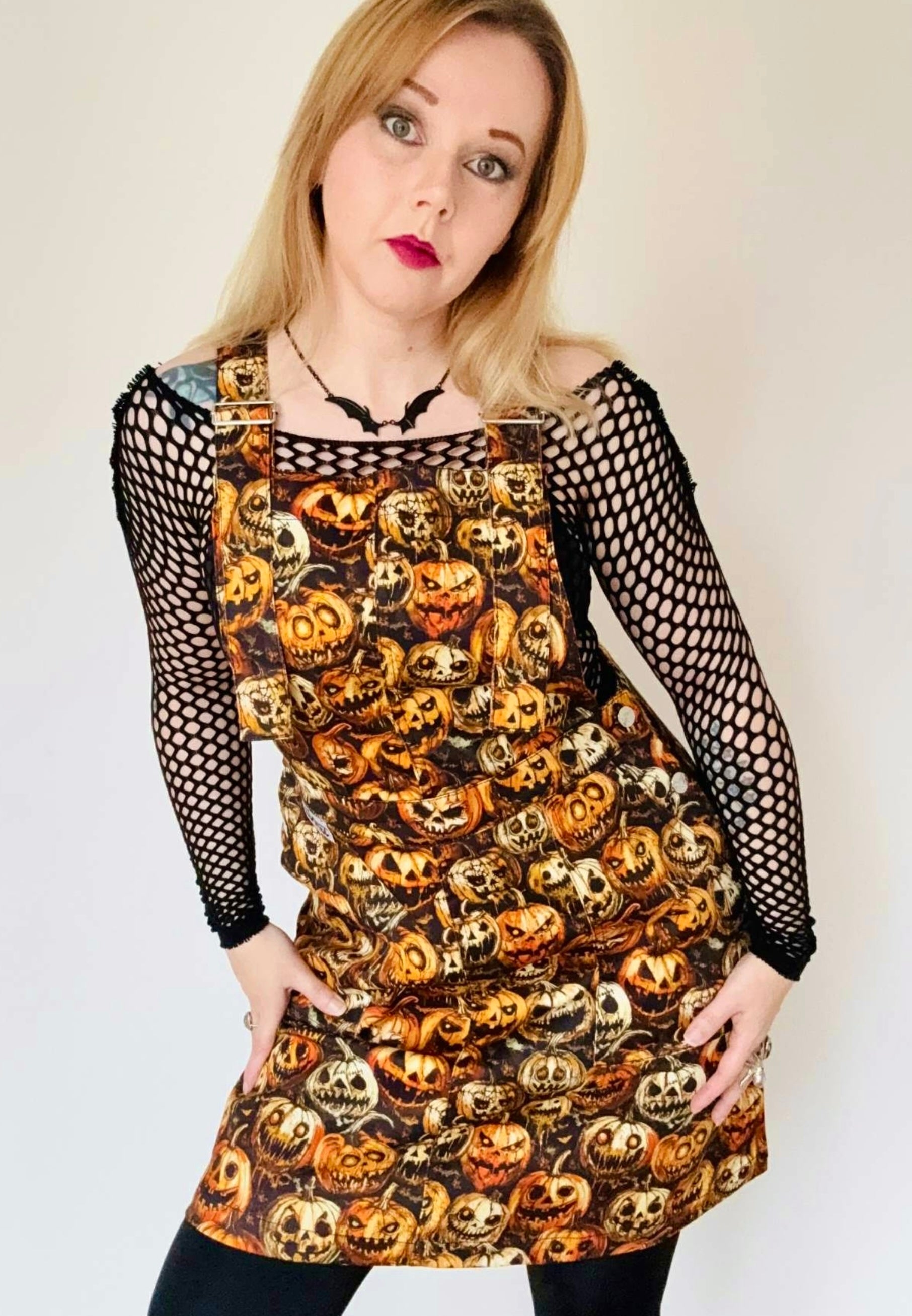Woman wearing a spooky pinafore dress with creepy pumpkins print. Studio photo. 