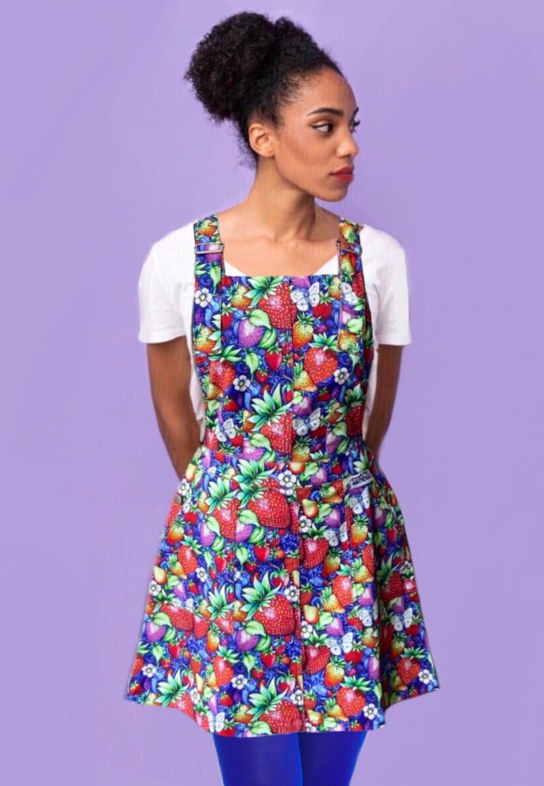 Woman wearing a beautiful pinafore dress with a vibrant wild strawberry print. 