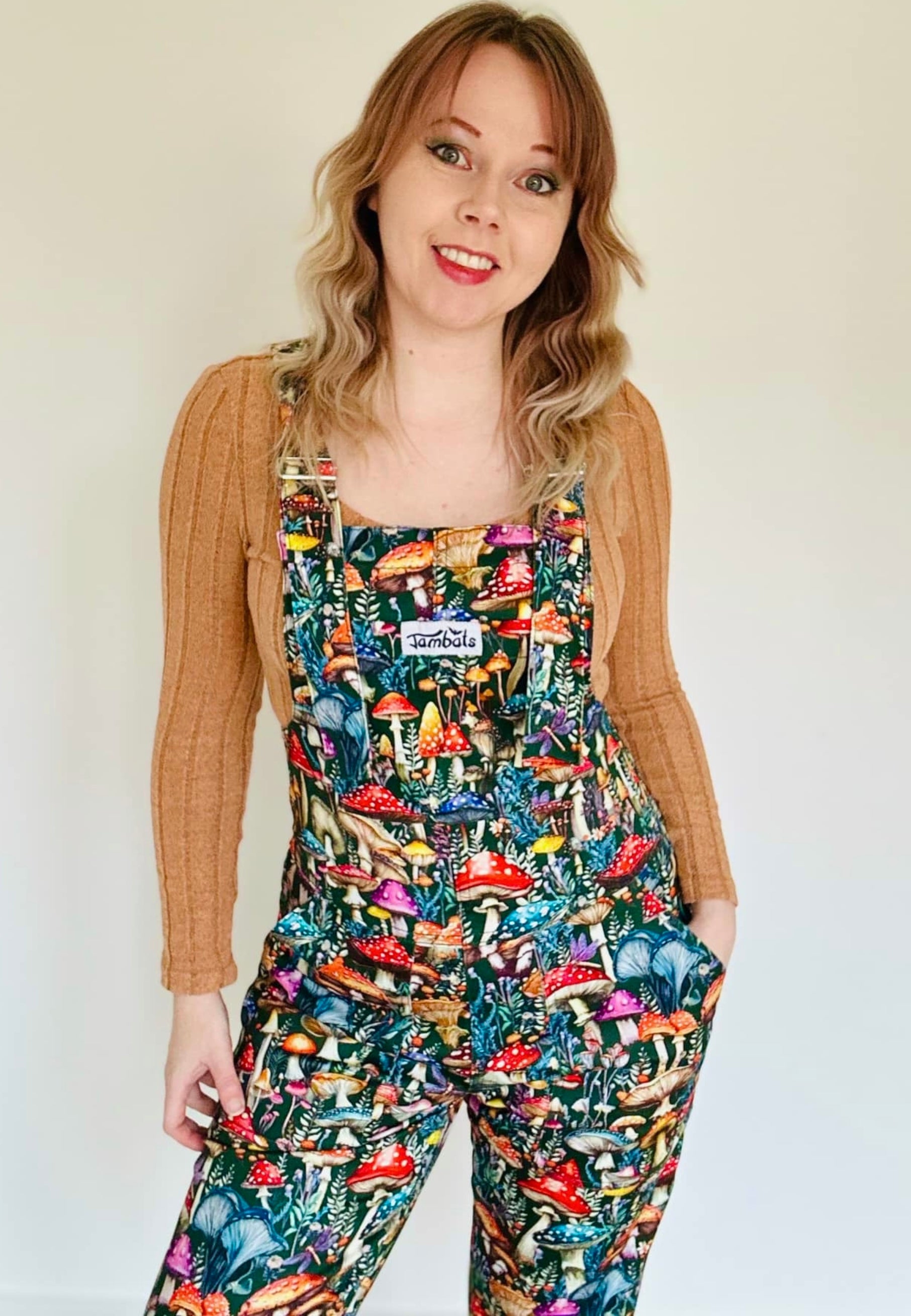 A person wearing a pair of vibrantly patterned dungarees with a beautiful mushroom design, standing against a plain background.