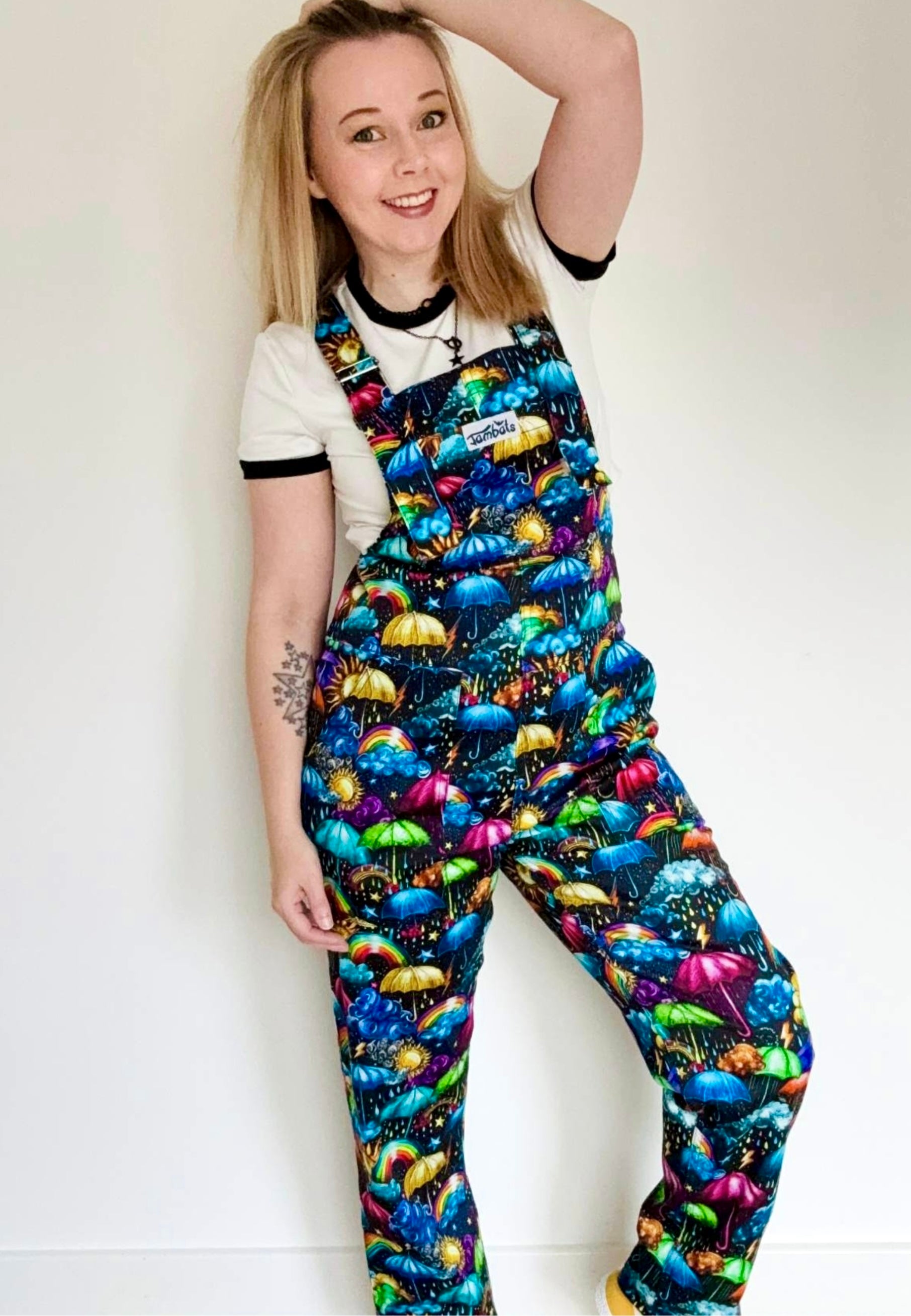 Woman wearing dungarees with a vibrant weather print. Whimsical fabric print of umbrellas, clouds, rain, sunshine, rainbows, storm clouds. Studio photo. 