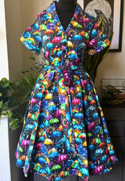 A beautiful shirt dress with a colourful weather print of umbrellas, sun, rain, rainbows, clouds. Displayed on a black dress mannequin indoors.