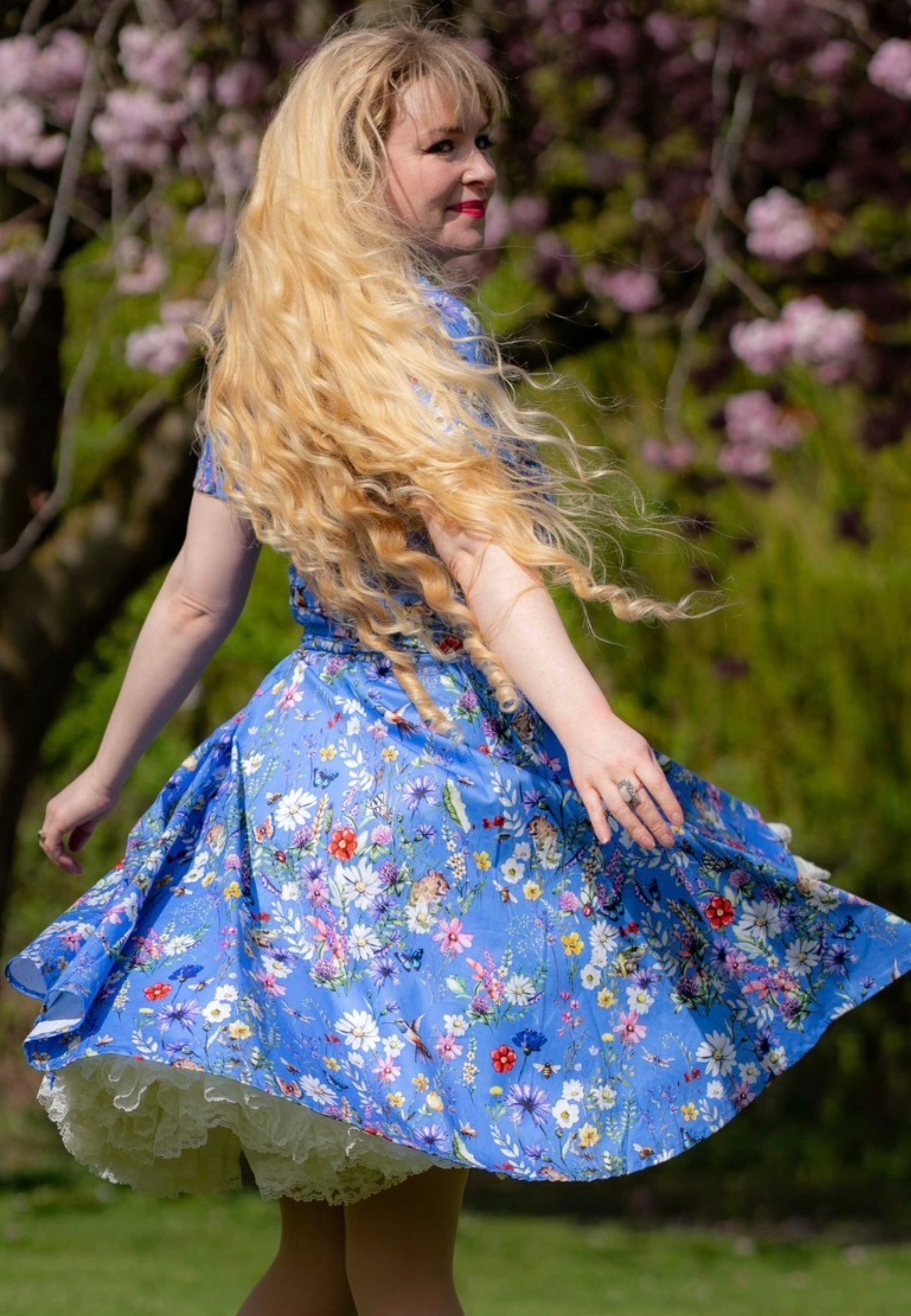 Woman in a beautiful cornflower blue floral dress standing outdoors twirling round with cherry blossoms in the background