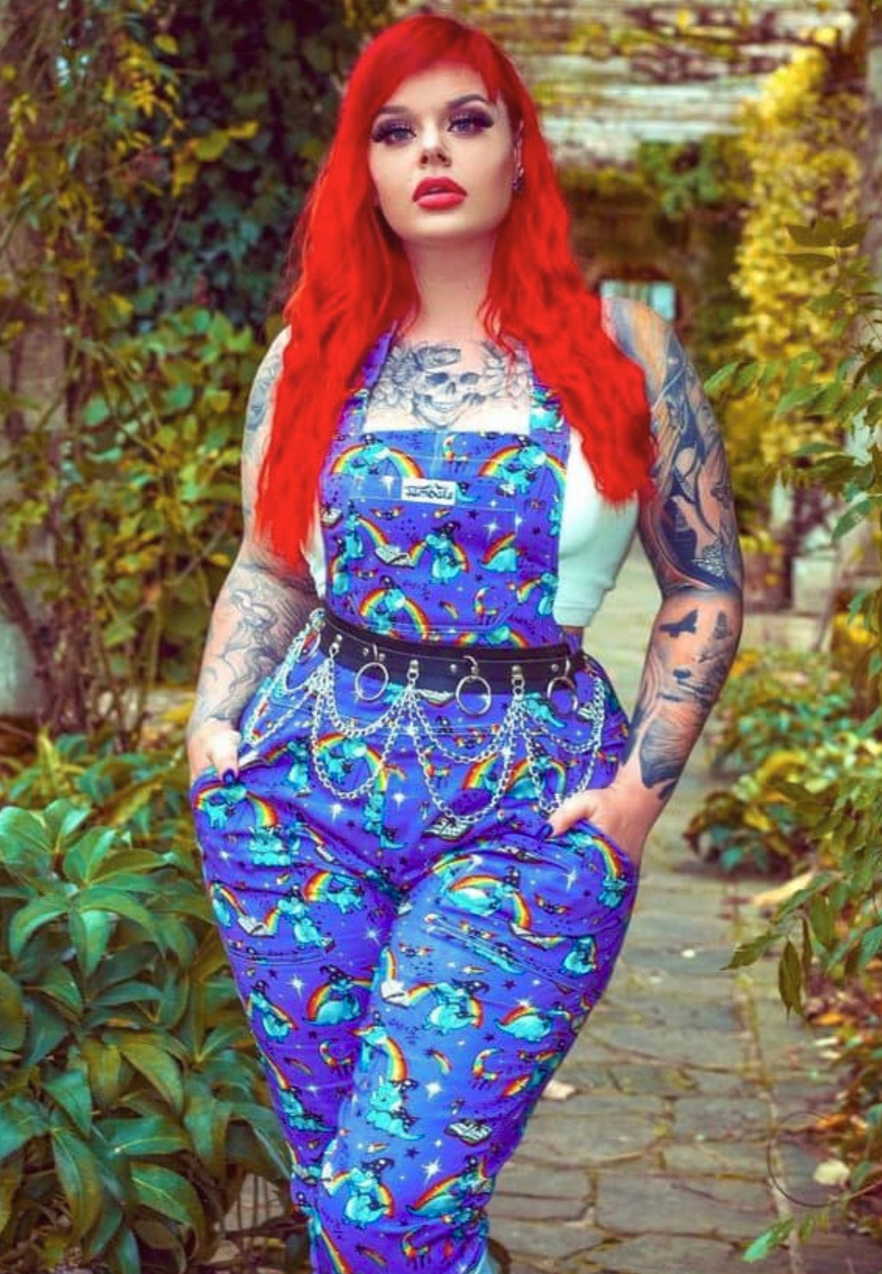 Red haired woman wearing purple dungarees with a print of wizard dinosaurs and rainbows and stars. Model is outdoors. 