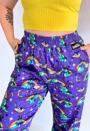 A person wearing purple trousers with a colourful print of wizard dinosaurs, rainbows, stars. Trousers are paired with a yellow ribbed crop top.
