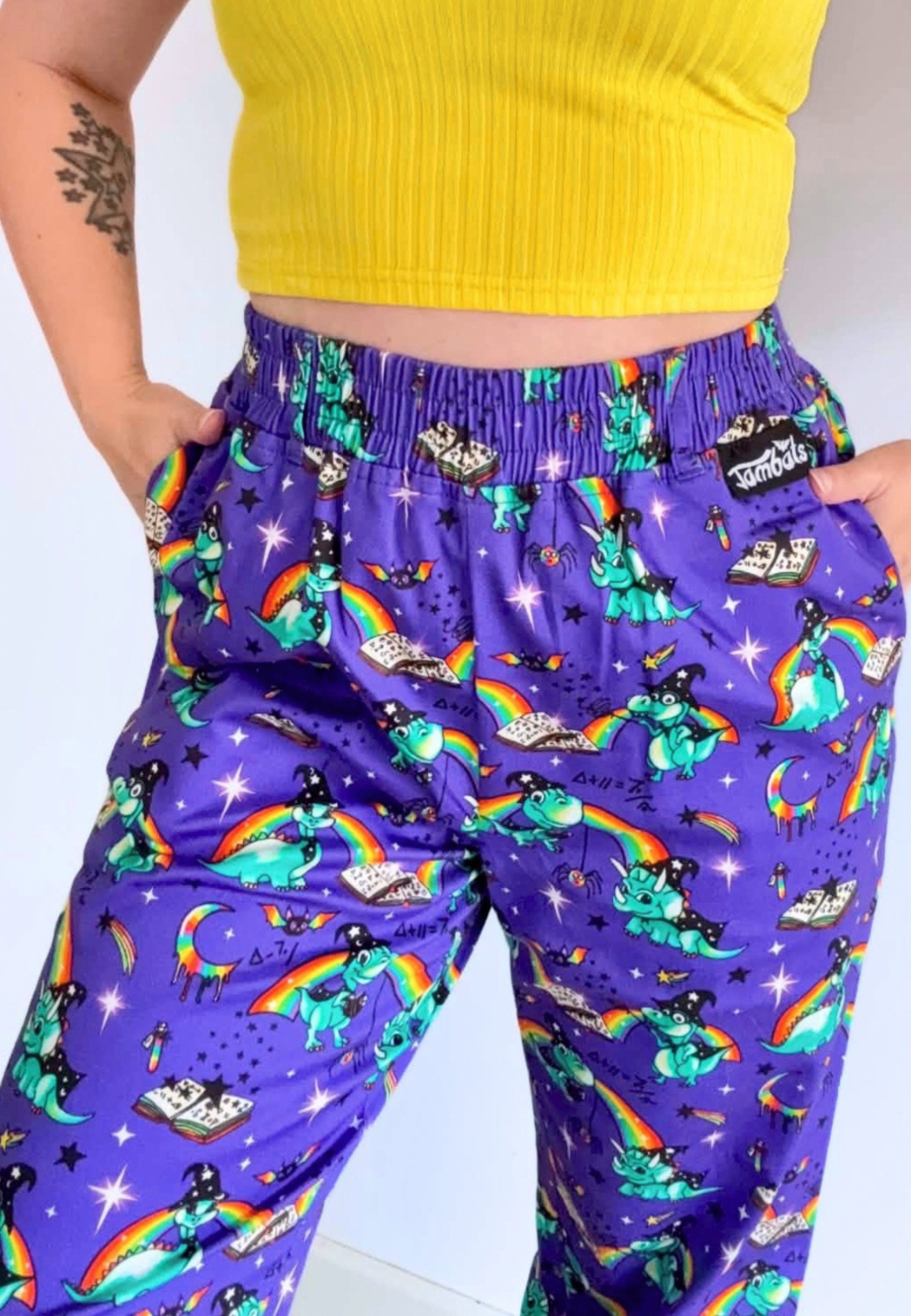 A person wearing purple trousers with a colourful print of wizard dinosaurs, rainbows, stars. Trousers are paired with a yellow ribbed crop top.