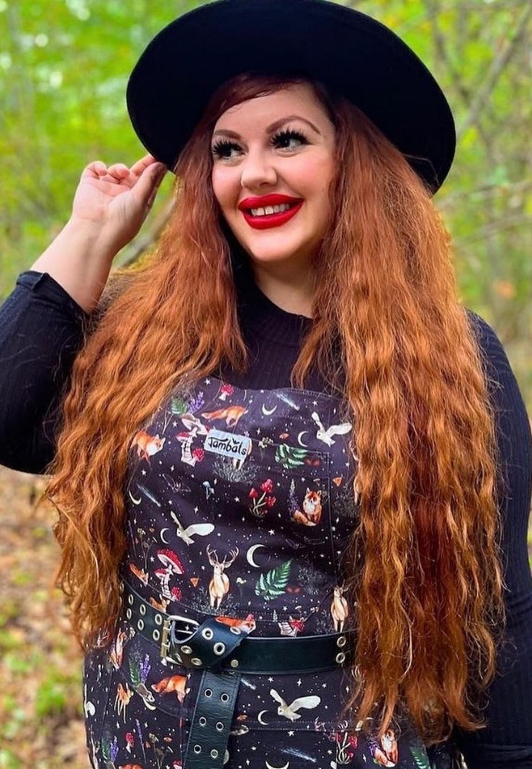Plus size model wearing Jambats Dark Forest dungarees. Black print with  moonlit forest, stars, shooting stars, moons and night dwelling creatures like owls, foxes, deer. Beautiful overalls