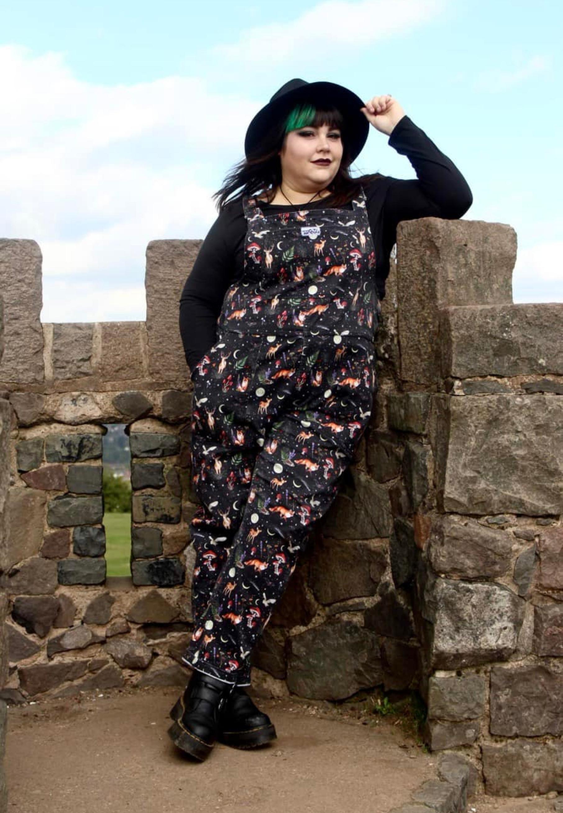 Plus size model wearing Jambats Dark Forest dungarees. Black print with  moonlit forest, stars, shooting stars, moons and night dwelling creatures like owls, foxes, deer. Beautiful overalls