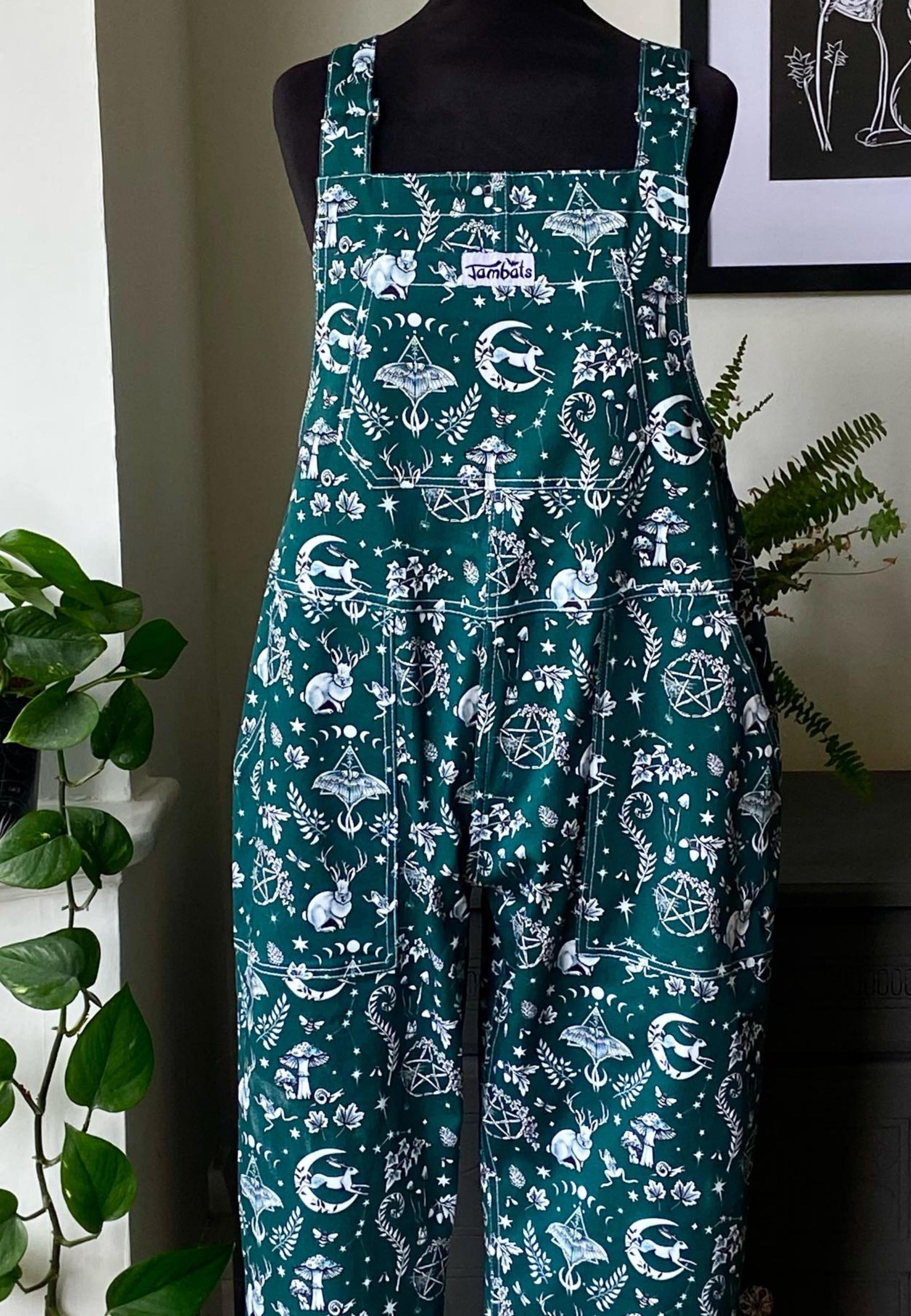 A mannequin photo of deep forest green dungarees with a unique illustrated mystical, natures magick print.